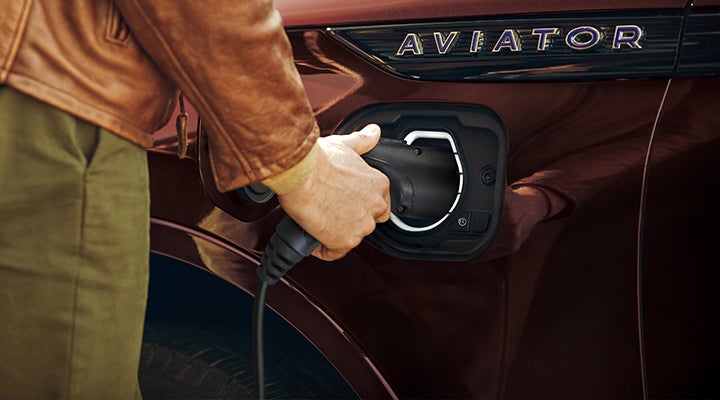 A hand is shown plugging a charger into the charging port of a 2023 Lincoln Aviator® Plug-in Hybrid model. | Irwin Lincoln in Freehold NJ