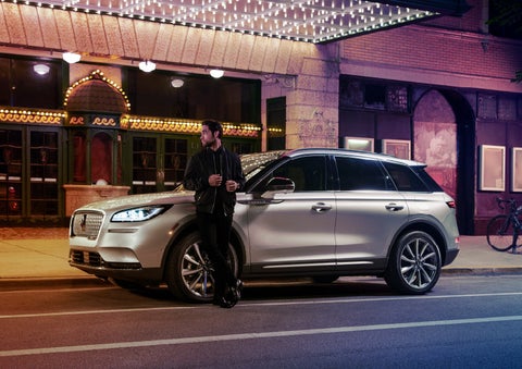A 2022 Lincoln Corsair SUV is parked outside a theater as the driver relaxes against the frame and lights illuminate the floating roofline and body | Irwin Lincoln in Freehold NJ