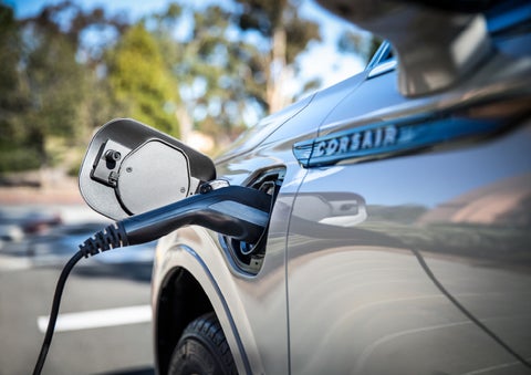A Lincoln electric charger is plugged into a 2022 Lincoln Corsair Grand Touring port as the body reflects the surroundings of a sun-soaked parking lot | Irwin Lincoln in Freehold NJ