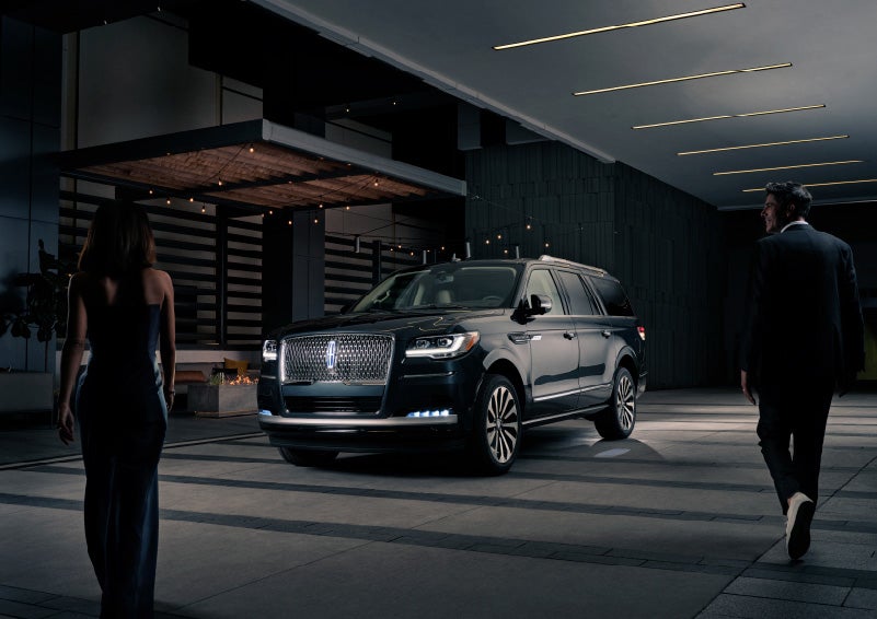 A man and woman in formal wear are approaching a 2022 Lincoln Navigator SUV at night as it lights with the Lincoln Embrace | Irwin Lincoln in Freehold NJ