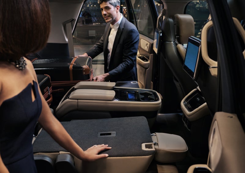 A man is pulling a suitcase out of the folded flat second-row of a 2022 Lincoln Navigator SUV | Irwin Lincoln in Freehold NJ