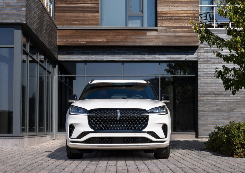 A white 2025 Lincoln Aviator® SUV is shown parked outside a modern building with gray brick and wood accents. | Irwin Lincoln in Freehold NJ