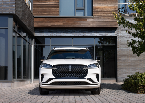 A white 2025 Lincoln Aviator® SUV is shown parked outside a modern building with gray brick and wood accents. | Irwin Lincoln in Freehold NJ