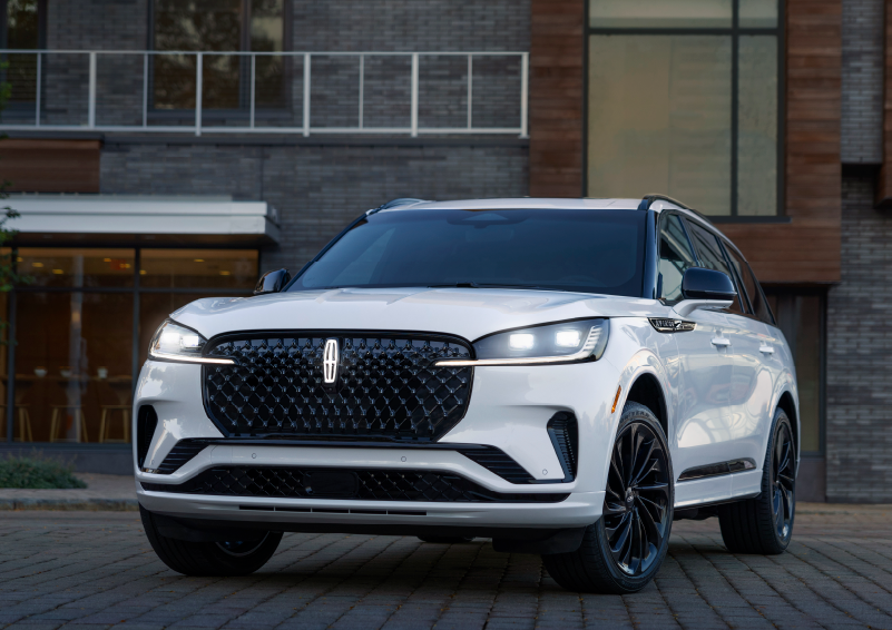 A white 2025 Lincoln Aviator® SUV is shown parked outside a modern building with gray brick and wood accents. | Irwin Lincoln in Freehold NJ