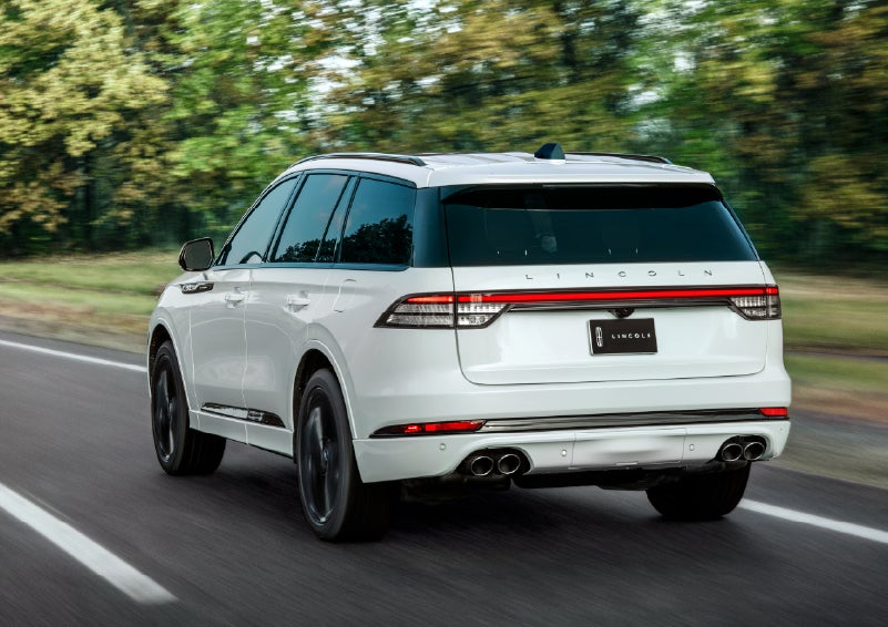 A white 2026 Lincoln Aviator® SUV is being driven away down a road lined with colorful trees. | Irwin Lincoln in Freehold NJ