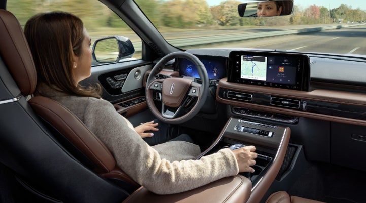 A 2027 Lincoln Aviator® SUV is being driven hands-free on a highway lined with trees. | Irwin Lincoln in Freehold NJ
