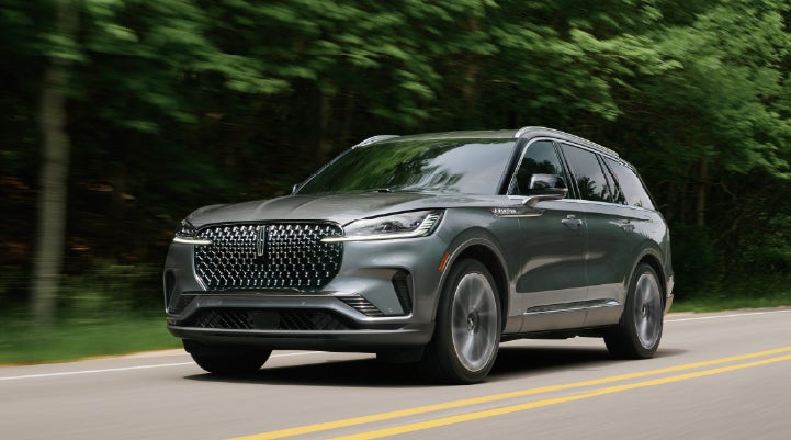 A 2027 Lincoln Aviator® SUV is being driven down a road lined with trees. | Irwin Lincoln in Freehold NJ